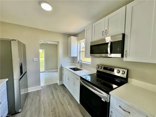 Kitchen featuring appliances with stainless steel finishes, white cabinetry, light wood finished floors, and light stone counters