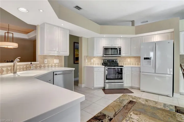 Kitchen featuring appliances with stainless steel finishes, sink, light tile patterned floors, white cabinetry, and hanging light fixtures
