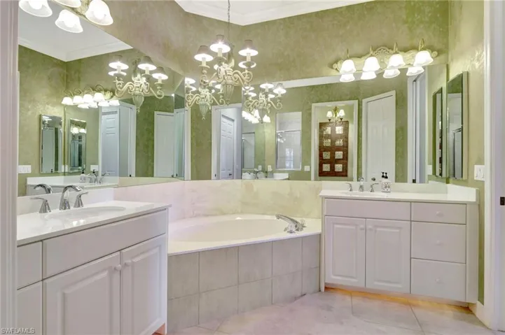 Master Bathroom featuring vanity, crown molding, an inviting chandelier, tile patterned flooring, and tiled bath