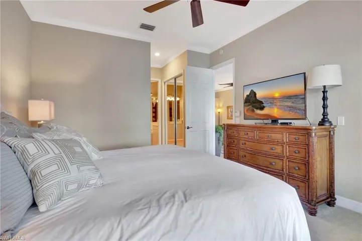 Master Bedroom featuring ensuite bath, ceiling fan, crown molding, light colored carpet, and two closets.