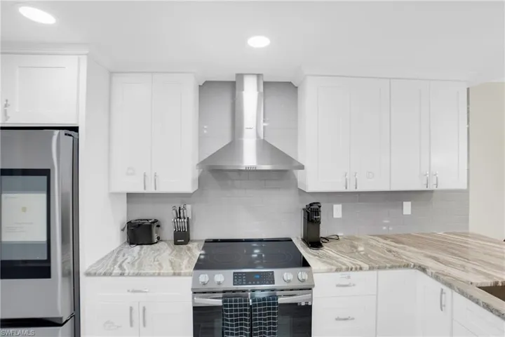 Kitchen featuring appliances with stainless steel finishes, wall chimney exhaust hood, light stone counters, white cabinets, and recessed lighting