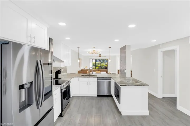 Kitchen with stainless steel appliances, white cabinets, a peninsula, decorative light fixtures, and a chandelier