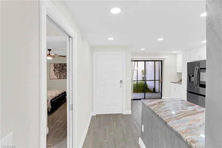 Kitchen featuring white cabinetry, stainless steel fridge, wood tiled floors, light stone countertops, and recessed lighting