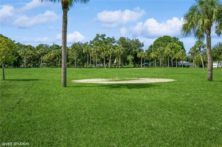 Expansive green lawn with a sand trap and flagstick, bordered by palm trees and mature foliage