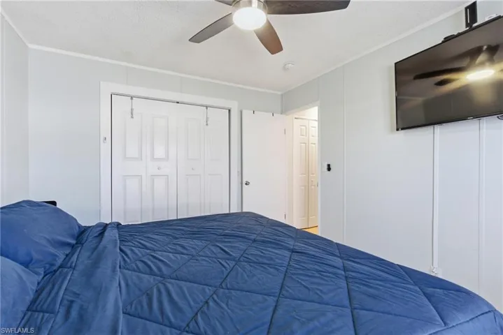Room featuring a ceiling fan with integrated lighting, wall-mounted television, white paneled walls, and bi-fold closet doors