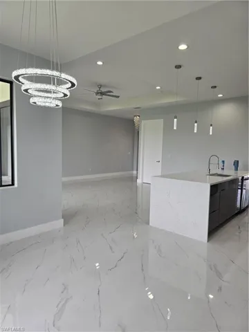 Kitchen with decorative light fixtures, ceiling fan with notable chandelier, an island with sink, sink, and light tile floors