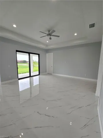 Unfurnished room featuring ceiling fan, a tray ceiling, and light tile floors
