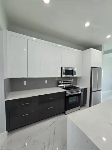 Kitchen featuring light stone countertops, white cabinets, range, and refrigerator