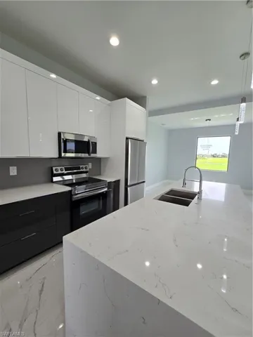 Kitchen featuring pendant lighting, stove, sink, white cabinets, and stainless steel refrigerator