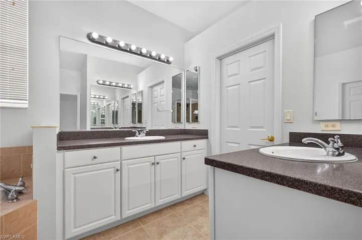 Dual vanity with integrated sinks, white cabinetry, dark speckled countertops, and a large wall-mounted mirror
