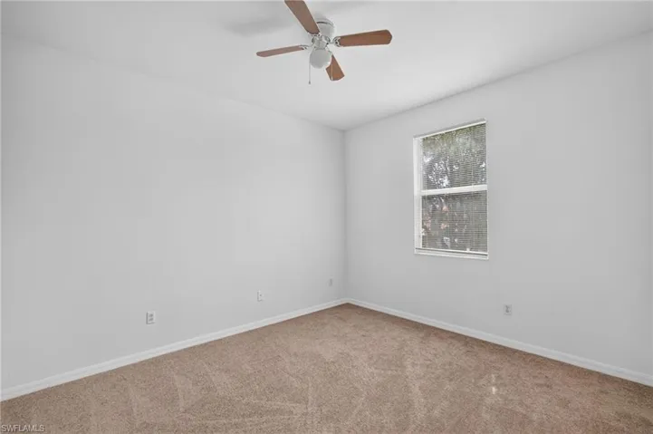 Neutral wall color, window with exterior scenery, ceiling fan with light fixture, and carpeted flooring