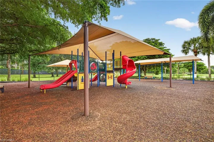 Playground area featuring multiple slides, swings, and shade canopies over a wood chip surface