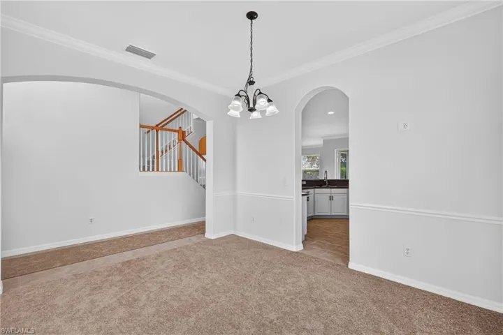 Neutral wall paint, crown molding, chair rail molding, arched doorways, and a chandelier with glass shades