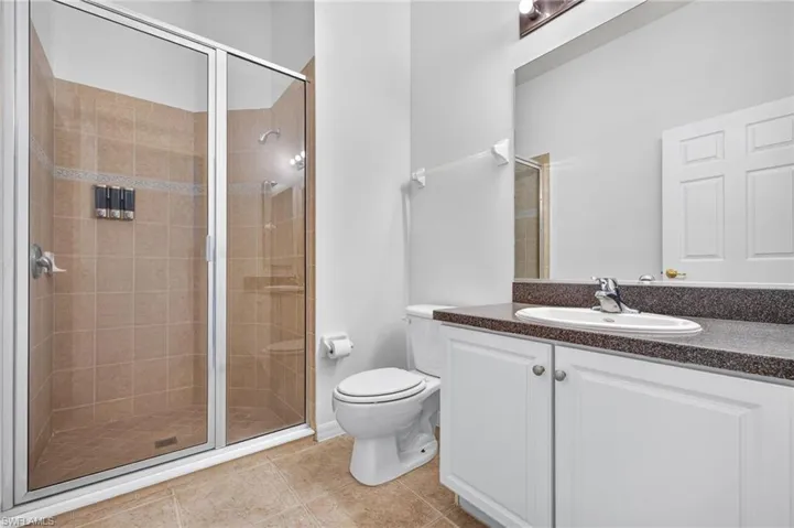 Glass-enclosed shower with tile surround, single vanity with integrated sink, white cabinetry, and a dark-speckled countertop