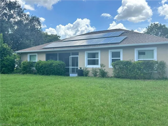 View of front of home with roof mounted solar panels, stucco siding, and a front yard