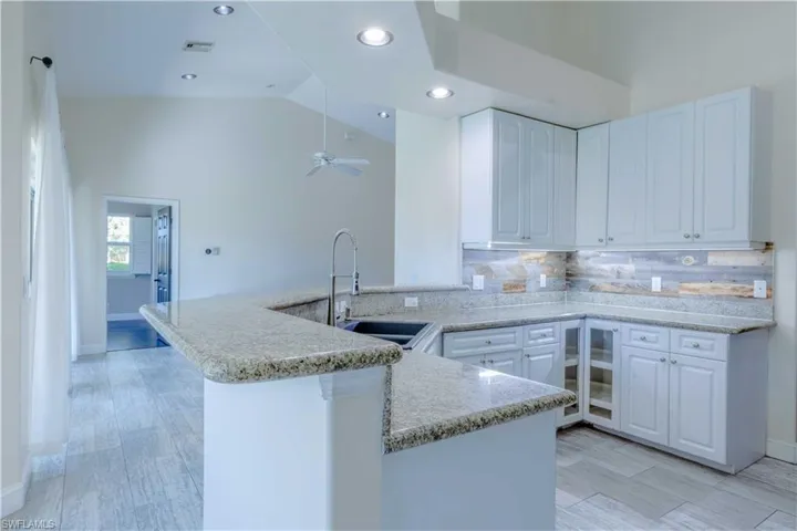 Kitchen featuring visible vents, white cabinets, a peninsula, vaulted ceiling, and a sink