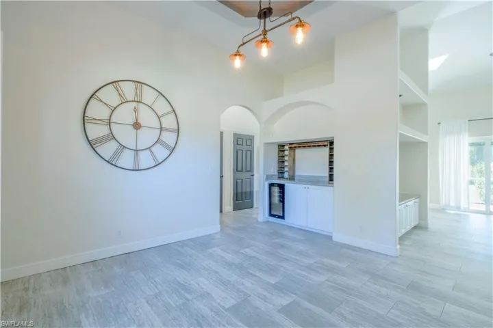 Unfurnished room with a high ceiling, beverage cooler, baseboards, and a dry bar