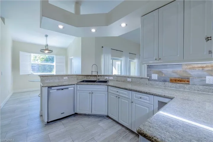 Kitchen featuring white cabinets, dishwashing machine, a sink, light stone countertops, and backsplash