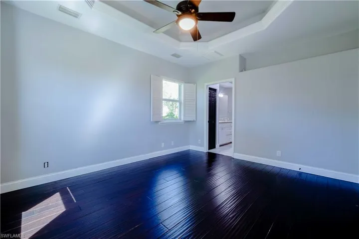 Unfurnished room featuring dark wood-style floors, a raised ceiling, visible vents, and baseboards