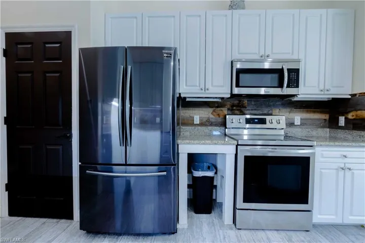 Kitchen with stainless steel appliances, light stone countertops, white cabinetry, and tasteful backsplash