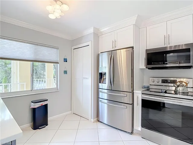 Kitchen featuring stainless steel appliances, white cabinetry with crown molding, white tile flooring, a built-in pantry, and a window with pleated blinds