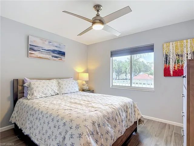 Bedroom featuring wood-finish flooring, a contemporary ceiling fan with integrated lighting, and a large window with blinds