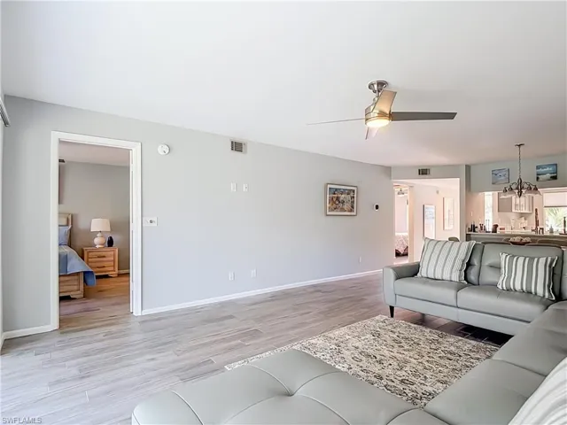 Spacious living area featuring wood-look tile flooring, light gray wall tones, and a ceiling fan with integrated lighting