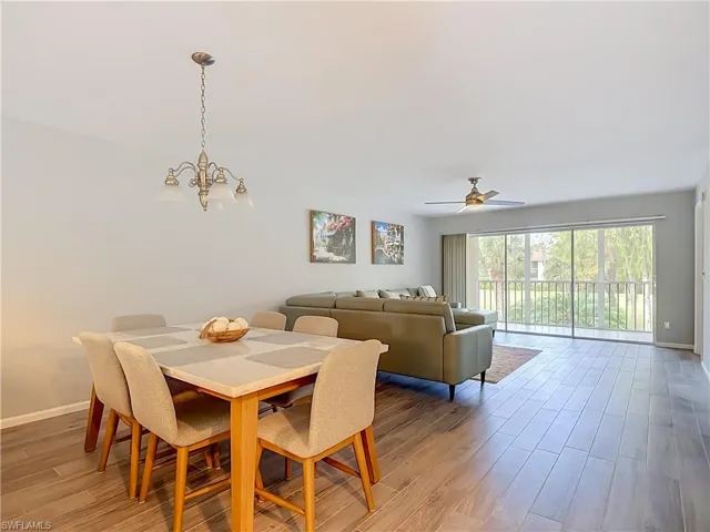 Open-concept living area featuring wood-finish flooring, a contemporary ceiling fan, and large sliding glass doors leading to an outdoor space with white railing