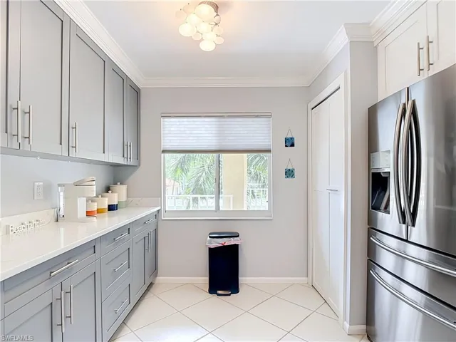 Modern kitchen featuring light gray cabinetry, white countertops, stainless steel refrigerator, and white tile flooring