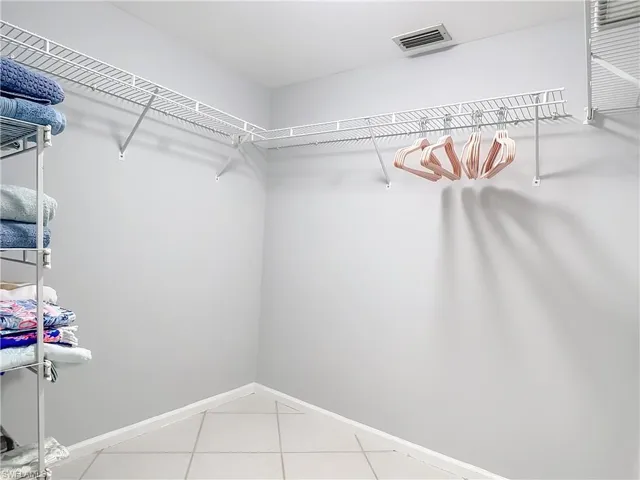 Walk-in closet featuring light gray walls, white wire shelving, a hanging rod, and light tile flooring