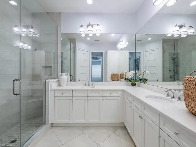 Bathroom with light tile patterned floors, a shower stall, two vanities, recessed lighting, and a chandelier