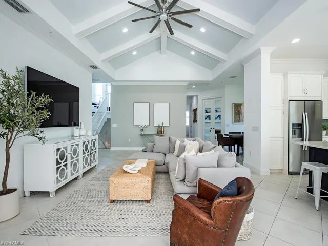 Living room featuring beamed ceiling, light tile patterned floors, a ceiling fan, stairs, and healthy amount of natural light