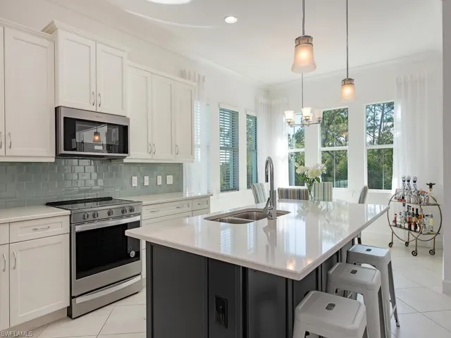 Kitchen featuring white cabinets, appliances with stainless steel finishes, dark cabinets, a kitchen island with sink, and light stone countertops