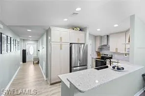 Kitchen featuring a peninsula, wall chimney range hood, a sink, light wood-style flooring, and appliances with stainless steel finishes