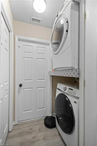Washroom with laundry area, a textured ceiling, wood finished floors, visible vents, and stacked washer and clothes dryer