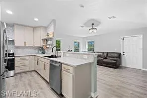Kitchen featuring appliances with stainless steel finishes, light wood-type flooring, light countertops, a sink, and a peninsula