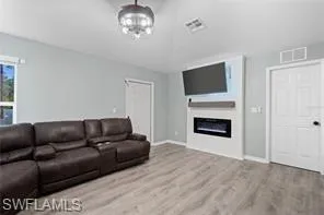 Living area with baseboards, visible vents, a glass covered fireplace, and wood finished floors
