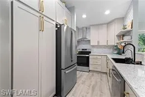 Kitchen featuring wall chimney range hood, appliances with stainless steel finishes, open shelves, light wood-type flooring, and a sink