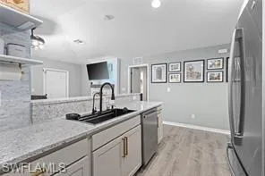 Kitchen featuring light stone countertops, open shelves, a sink, stainless steel appliances, and light wood-style flooring