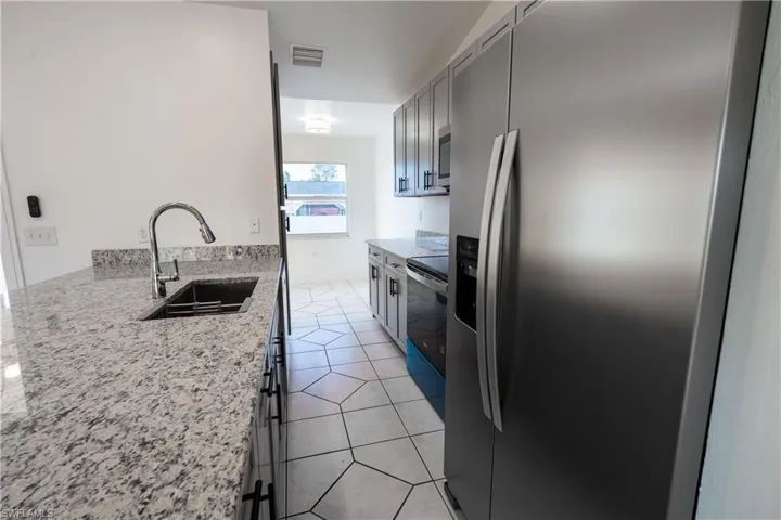 Kitchen featuring stainless steel appliances, light granite countertops, light tile patterned flooring, and gray cabinets