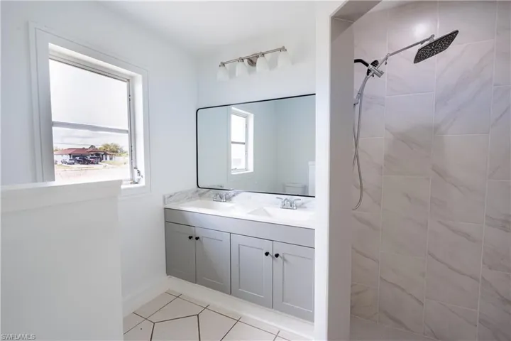 Bathroom featuring tiled shower, double vanity, and light tile patterned floors