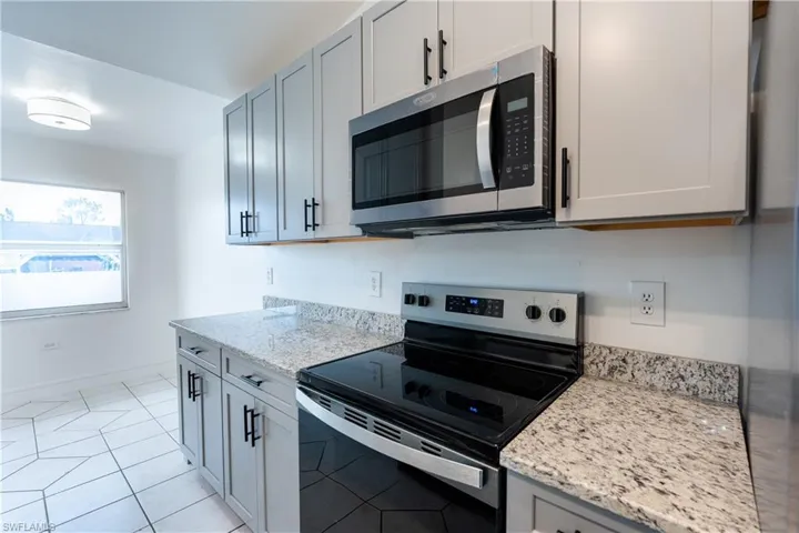 Kitchen featuring stainless steel appliances, light granite countertops, light tile patterned floors, and gray cabinets