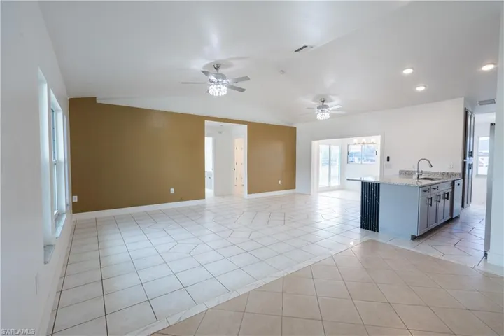 Kitchen with open floor plan, light stone counters, vaulted ceiling, a peninsula, and ceiling fan