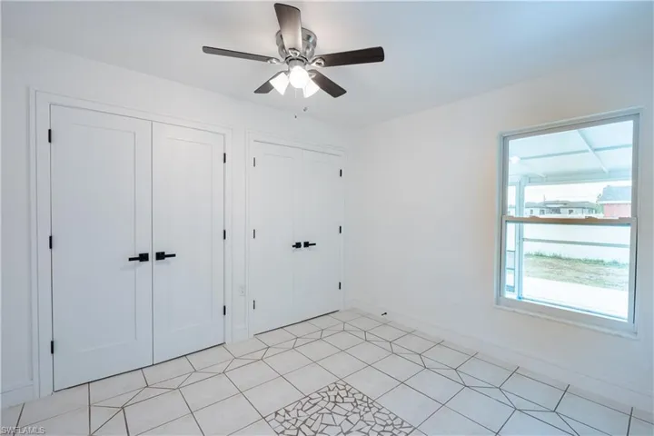 Unfurnished guess bedroom with two closets, ceiling fan, and light tile patterned floors