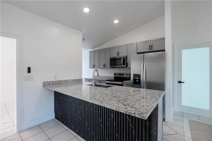 Kitchen featuring stainless steel appliances, a peninsula, light granite counters, lofted ceiling, and light tile patterned floors