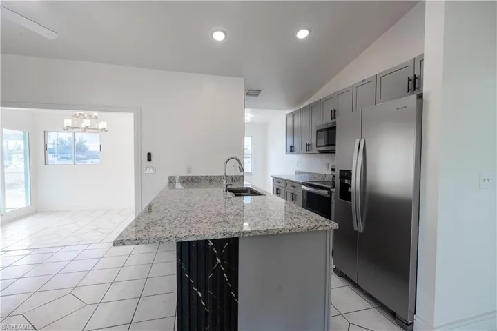 Kitchen featuring stainless steel appliances, light stone counters, a peninsula, gray cabinetry, and lofted ceiling