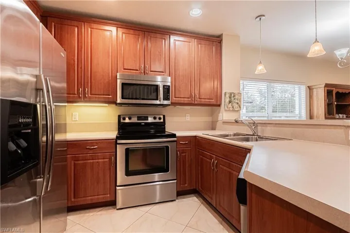 Kitchen featuring stainless steel appliances, light tile patterned floors, hanging light fixtures, and sink