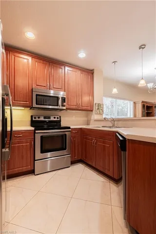 Kitchen featuring sink, light tile patterned floors, hanging light fixtures, and appliances with stainless steel finishes