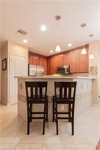 Kitchen with appliances with stainless steel finishes, hanging light fixtures, kitchen peninsula, a breakfast bar, and light tile patterned flooring