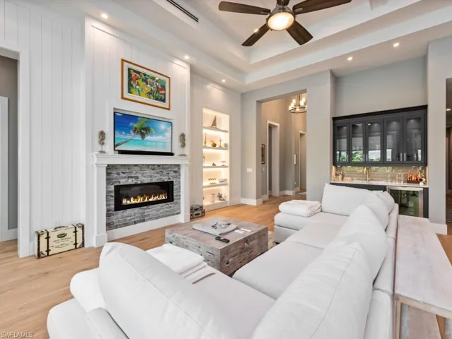 Living room with light hardwood / wood-style flooring, beverage cooler, ceiling fan with notable chandelier, built in shelves, and a fireplace
